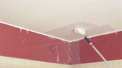 Een stukadoor brengt voorstrijk aan op een plafond met een roller op een telescoopsteel.