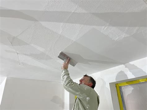 Een stukadoor egaliseert vers aangebracht stucwerk op een plafond met een afrijlat.