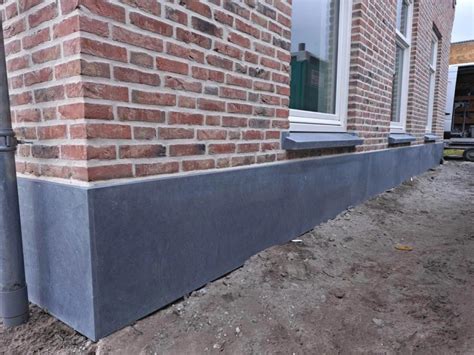 Een gevel met een natuurstenen borstwering en raamdorpels die de architectuur accentueren.