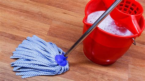 Afbeelding van iemand die een tegelvloer reinigt met een dweil en een emmer.