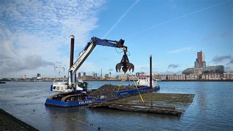 Foto van een kraanschip dat werkzaamheden uitvoert in een haven, zoals het plaatsen van steigerpalen.