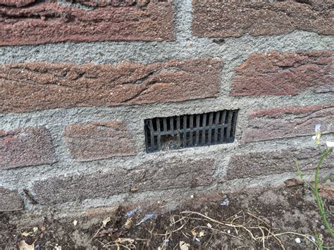 Een ventilatierooster in een buitenmuur, zichtbaar vanaf de kruipruimte