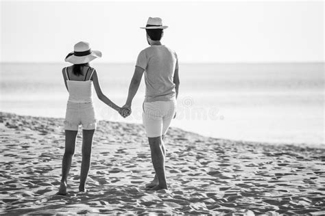Een bruidspaar dat lachend hand in hand loopt op een strand, met de zon op de achtergrond.