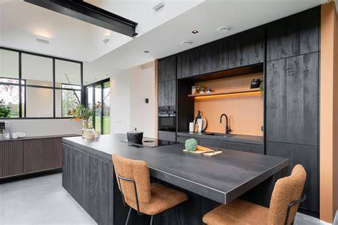 Afbeelding: Betonlook en bronzen/gouden accenten in een moderne keuken, met een sleek kookeiland en greeploze fronten