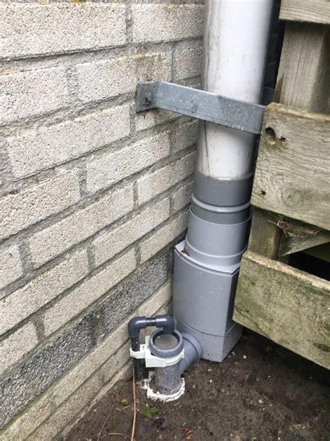 Foto van een witte regenpijp die aansluit op een regenton.