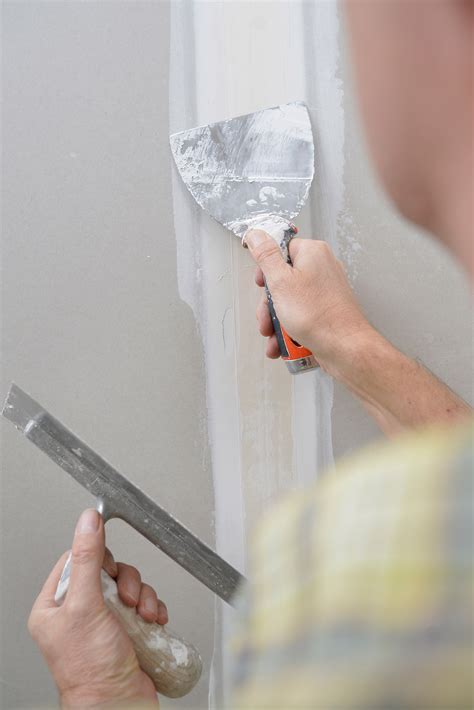 Een stukadoor brengt vulmiddel aan in een gipsplaat naad met een holle spaan en stuctroffel.