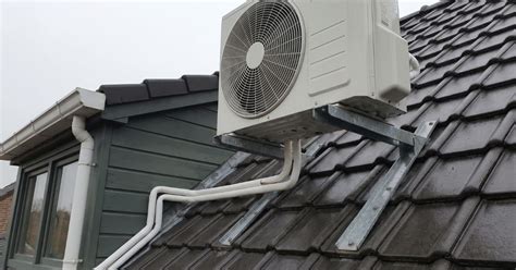 Een afbeelding van een dakkapel met buitenunit op de rand van het dak, omgeven door groen en een heldere lucht