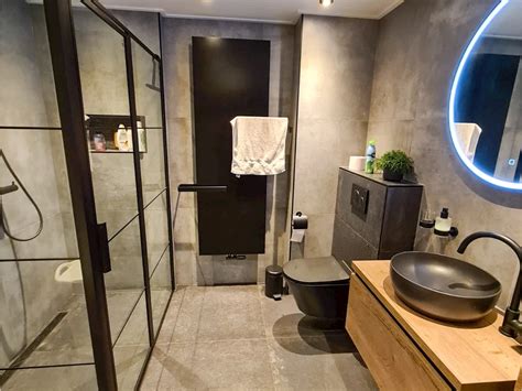 Een voorbeeld van een industriële badkamer met betonlook tegels, stalen elementen en een houten wastafelmeubel.
