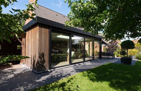 Foto van een moderne houten aanbouw met grote raampartijen en openslaande deuren.