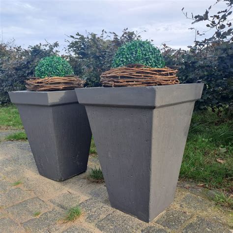 Een strakke, moderne betonnen vaas geplaatst in een tuinsetting.